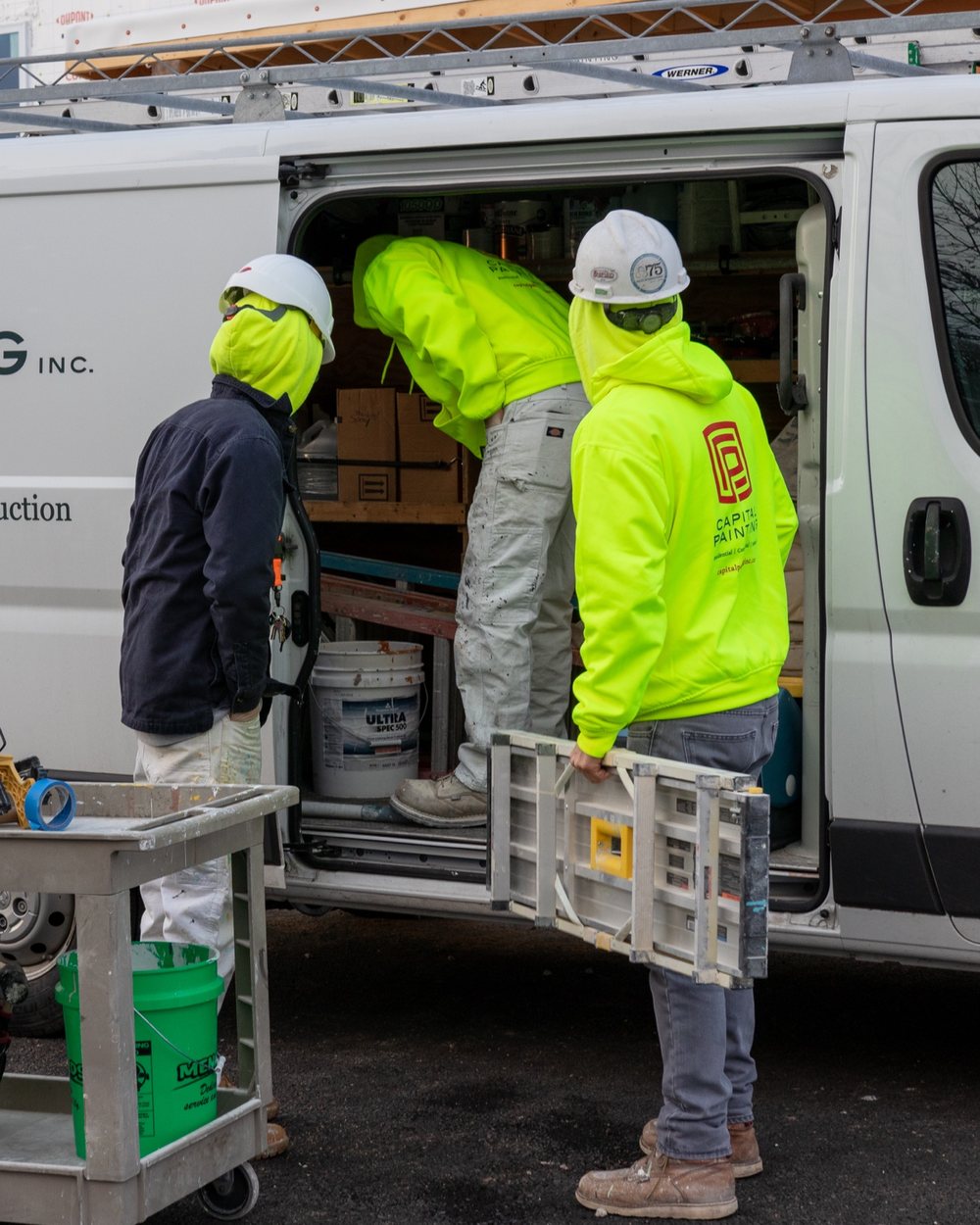 Capital Painting crew in branded hi-vis sweatshirts loading equipment from a company van